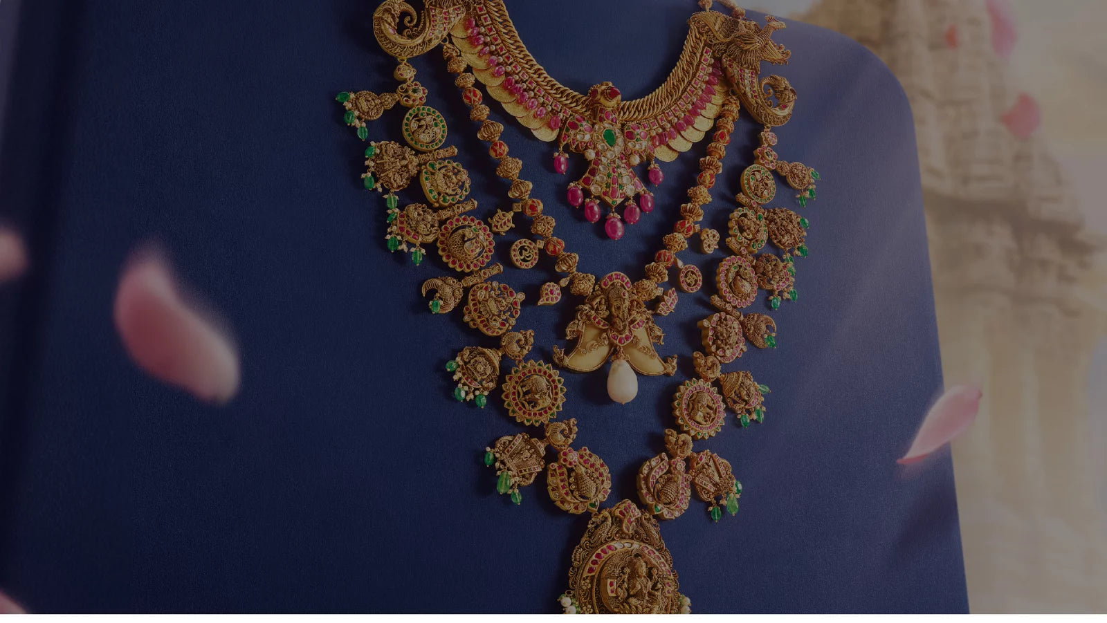 Intricate Indriya gold necklaces with ruby and emerald accents on midnight-blue fabric